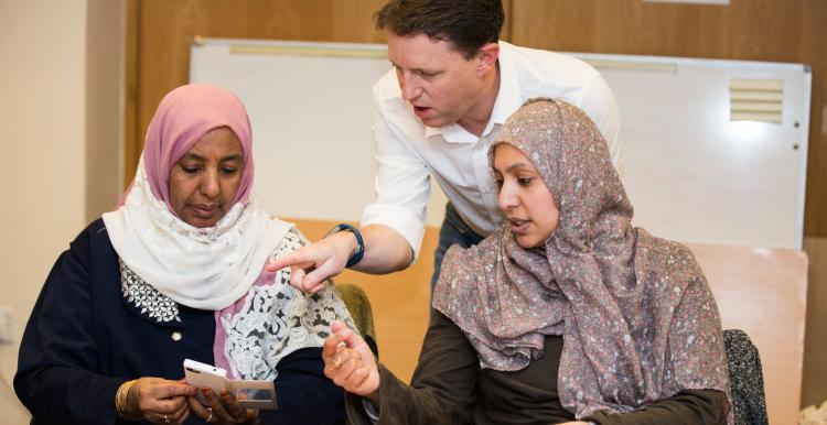 image of a man traing two women on use of an application on their mobile telephone